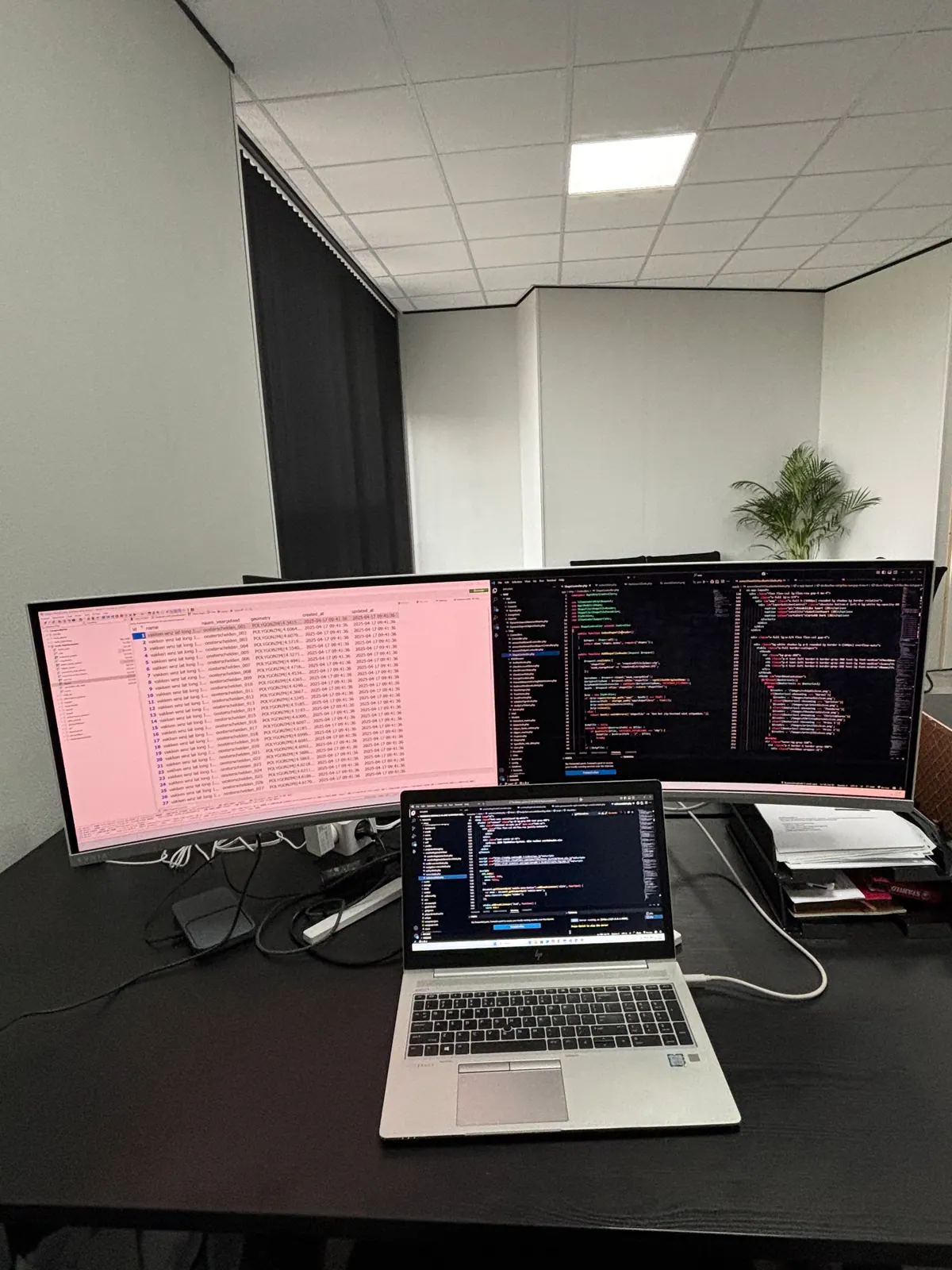 Werkplek van een ontwikkelaar met laptop en breedbeeldscherm met code